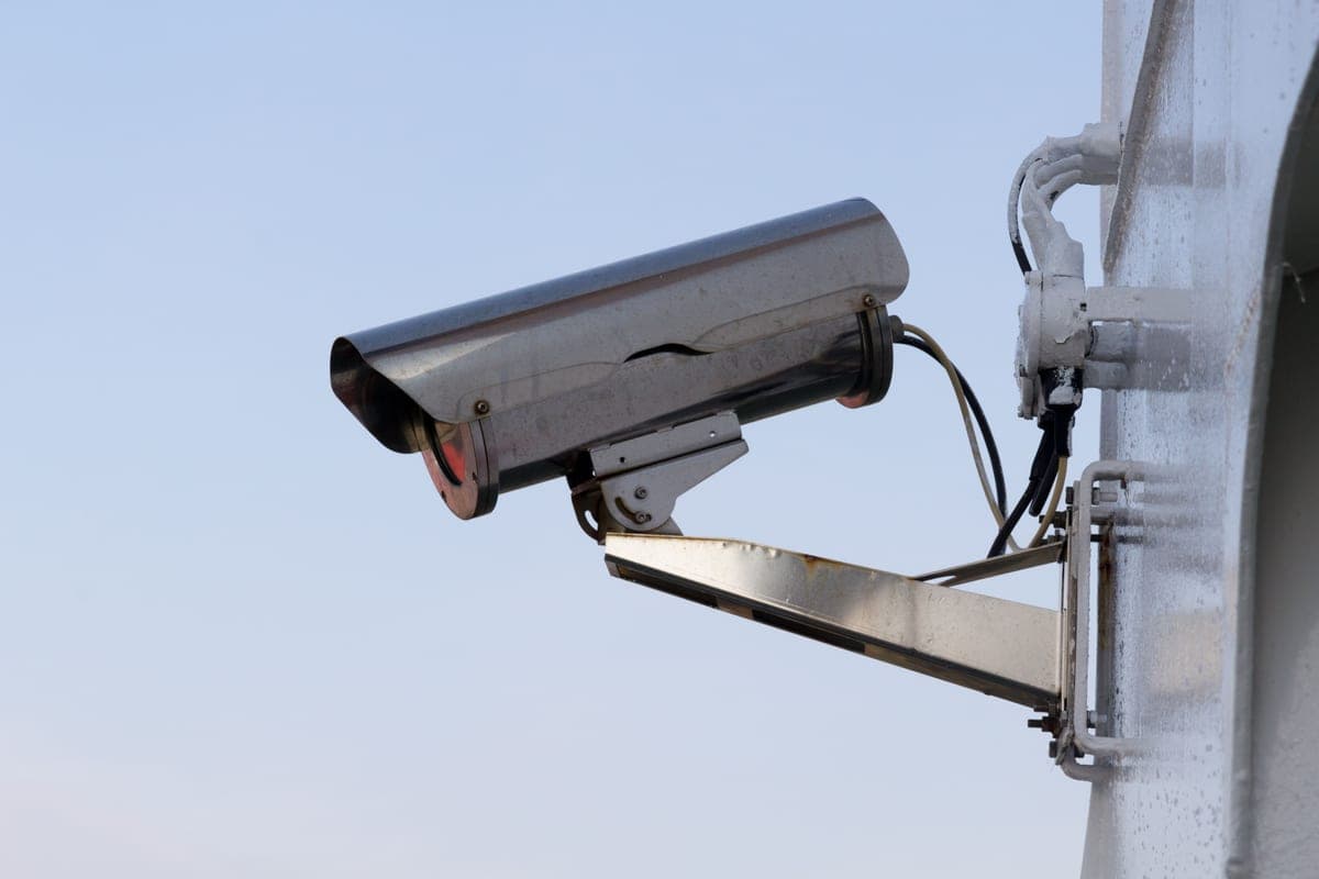 A small security camera mounted on the exterior wall of a home in daylight